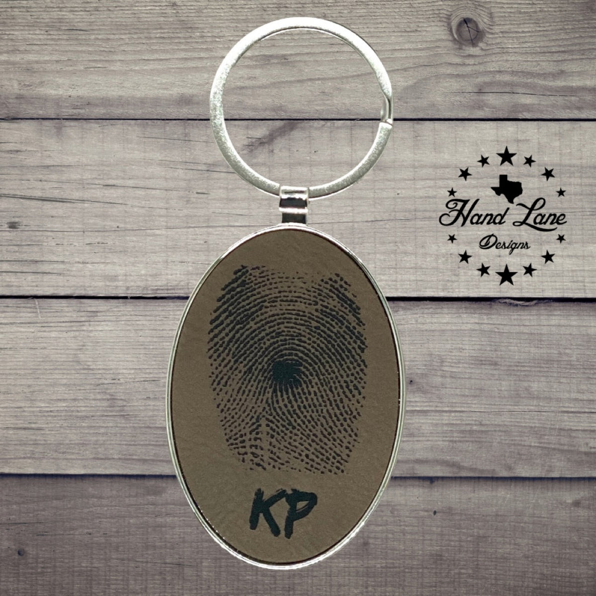 Dark brown oval leatherette keychain laser engraved with a fingerprint and initials, silver frame