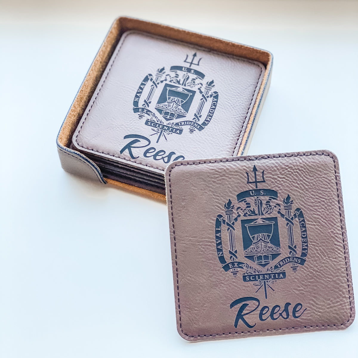Square leatherette coasters engraved with US Naval Academy crest and name Reese, one propped against the holder set