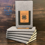 Custom engraved 4-H leatherette journal displayed on a stack of gray notebooks
