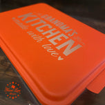 Orange cake pan lid laser engraved Grandma's Kitchen Made with Love, angled close-up on the design