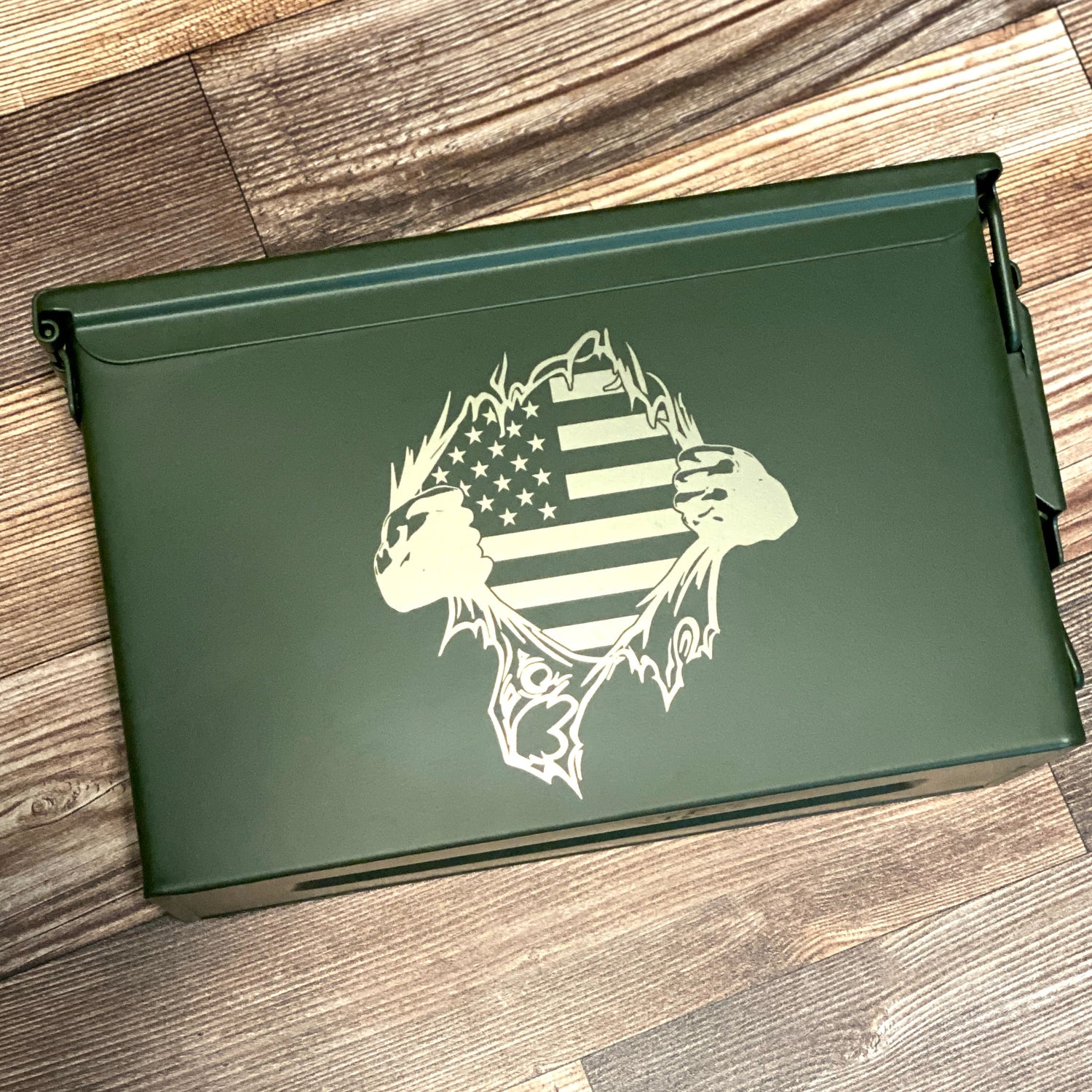 Olive green 50 cal ammo can lid engraved with hands tearing open to reveal an American flag design